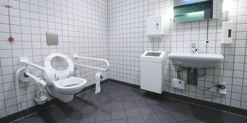 Eine klassische öffentliche Behindertentoilette mit relativ viel Raum und zwei Haltegriffen neben dem Klo