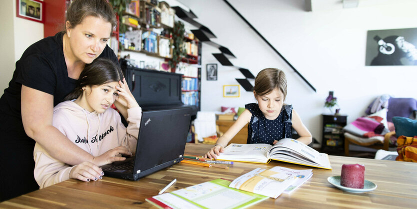 Eine Frau mit Kindern beim Homeschooling am Küchentisch.