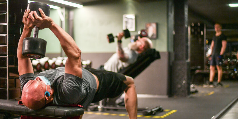 Ein Mann liegt auf einer Bank im Fitnessstudio und stemmt eine Hantel