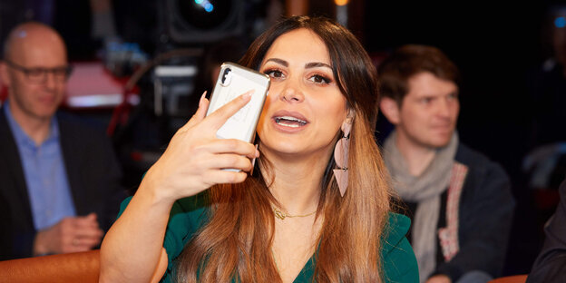 Enissa Amani mit einem Smartphone in einer Talkshow.