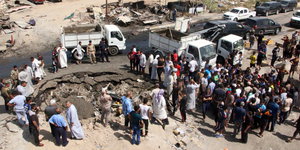 Iraker stehen um ein Erdloch, das durch eine Bombenexplosion entstanden ist.