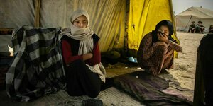 Zwei verschleierte Mädchen sitzen im Eingangsbereich eines Zeltes in einem Camp