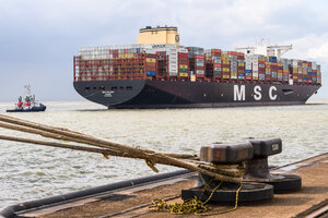 Ein voll beladenes Containerschiff wird von Schleppern an eine Kaje manövriert
