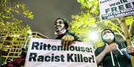 Eine Frau hält ein Plakat mit der Aufschrift "Rittenhouse Racist Killer", im Hintergrund: von Laternenlicht angestrahlte Bäume