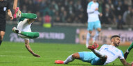 Ein Spieler von Werder Bremen fliegt gerade durch die Luft, ein Spieler von schlake 04 liegt auf dem Rasen