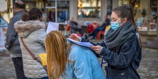 Impfwillige in einer Warteschlange, eine Frau füllt ein Formular auf dem Rücken einer anderen Frau aus