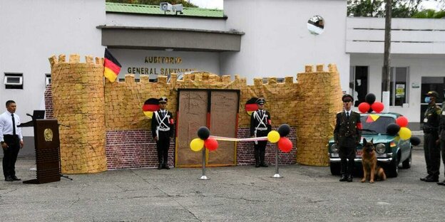 Vor dem Eingang der Polizeisschule steht ein als Adolf Hitler verkleideter Mann mit Schäferhund, daneben Luftballons in Schwarzrotgold