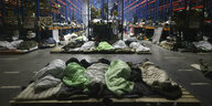 Menschen liegen auf Paletten mit Schlafsäcken zwischen Regalen