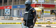 ein bewaffneter Polizist mit Schutzkleidung steht vor einer Absperrung