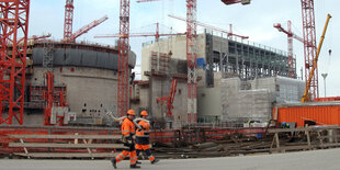 Zwei Arbeiter vor einer Baustelle. Im Hintergrund sieht man Baukräne und Betonblöcke.