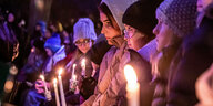 Frauen stehen mit Kerzen in der Hand in einer Reihe der Trauernden