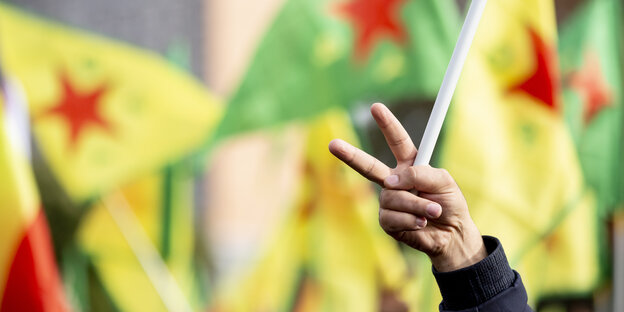 Ein Victorie Zeichen, im Hintergrund sind mehrere verschwommene Flaggen der syrischen kurdischen Partei