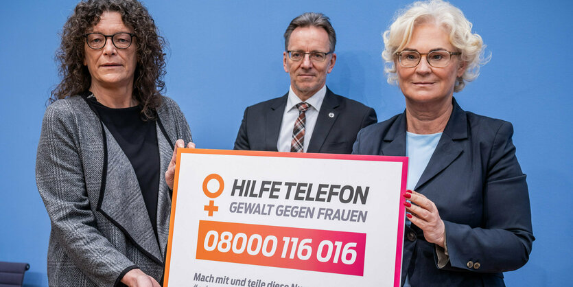 2 Frauen halten ein Schild mit der Nummer des Hilfetelefons hoch