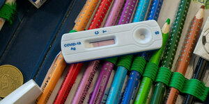 Das Bild zeigt einen Corona-Teststreifen, der auf Stiften in einem Schuletui liegt.