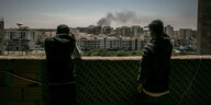 Vertriebene Männer beobachten aufsteigenden Rauch aus dem bombardierten Stadtviertel Bou-Selim.