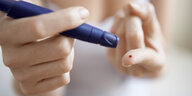 Blutstropfen auf einem Finger, diabetes Meßgerät in der anderen hand