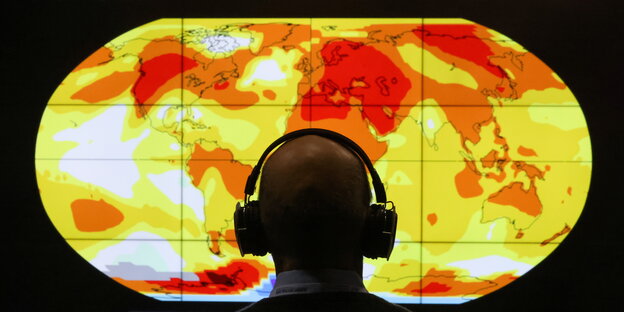 Mann mit Kopfhörern sitzt vor einer Weltkarte zu Temparturen