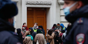 Menschen drängen sich vor einer Tür, rechts und links russische Polizisten