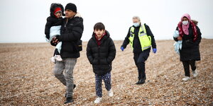 Ein Mann trägt ein Kind auf den Armen, neben ihm läuft ein kleiner Junge, dahinter ein Grenzbeamter und eine Frau