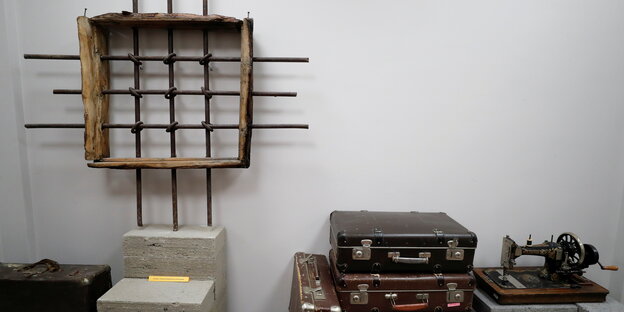 Ausstellungsstück:Ein Fenster mit Gitterstäben erinnert an ein Gefängnis, daneber Koffer und eine Nähmaschine