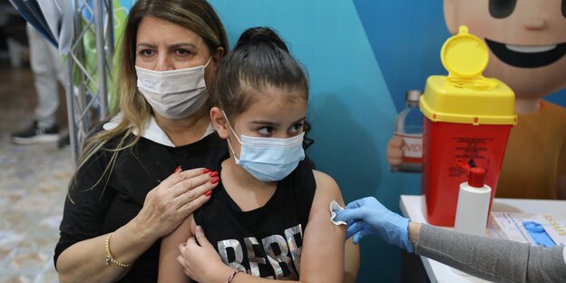 Ein Mädchen auf dem Schoß ihrer Mutter bekommt eine Impfung