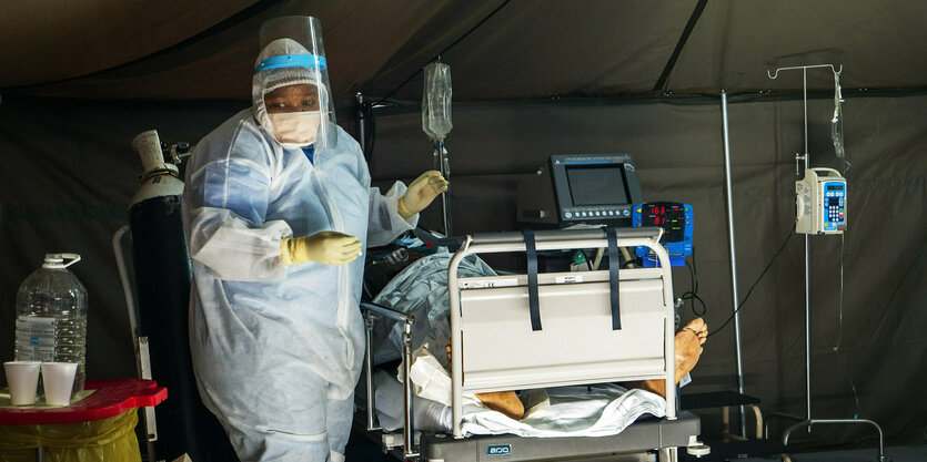 Gesundheitspersonal in Schutzanzug neben Krankenbett