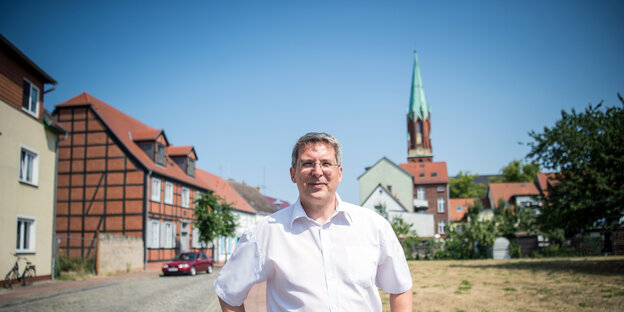 Ein Mann in weißem Hemd steht vor einer Kleinstadt mit Kirchturm