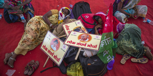Frauen in indischen Gewändern liegen und sitzen zwischen Fahnen, Plakaten und Gepäck.