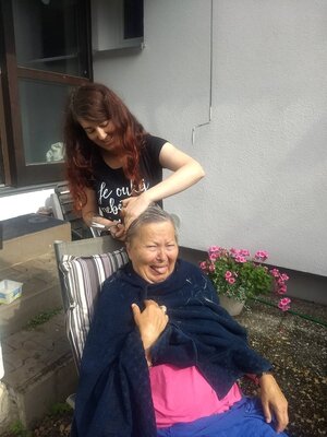 Eine alte und eine junge Frau, die junge schneidet der alten die Haare Eine alte und eine junge Frau, die junge schneidet der alten die Haare