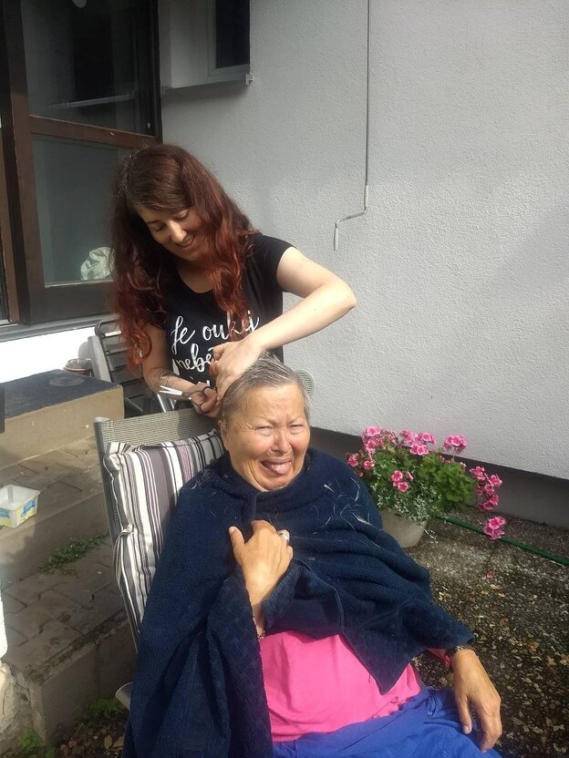 Eine alte und eine junge Frau, die junge schneidet der alten die Haare