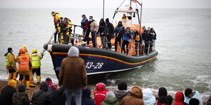Ein Rettungsboot setzt Menschen an einem Strand ab.