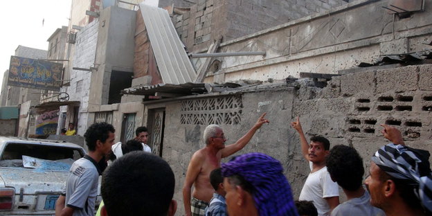 Menschen zeigen auf ein zerstörtes Gebäude im Jemen