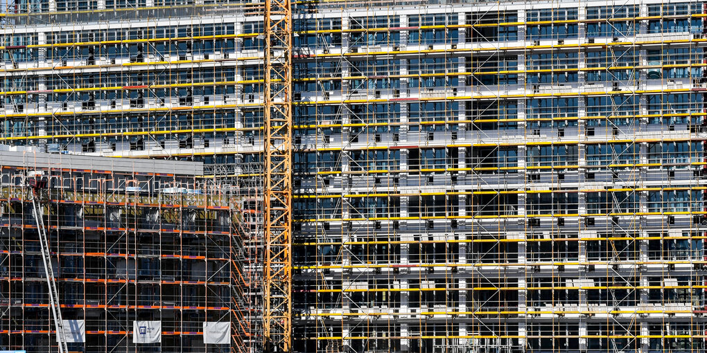 Eine eingerüstete Häuserfassade eines mehrstöckigen Büroneubaus, der hauptsächlich aus Glas und Beton besteht