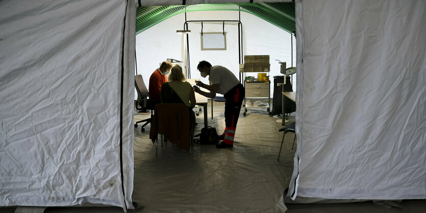 Blick in ein Impfzelt,2 Personen sitzen am Tisch, eine Person beugt sich mit einer Spritze über eine Sitzende