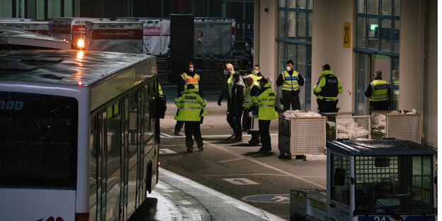 Ein Mann wird durch ein Spalier von Polizisten und Polizistinnen zu einem Bus gebracht