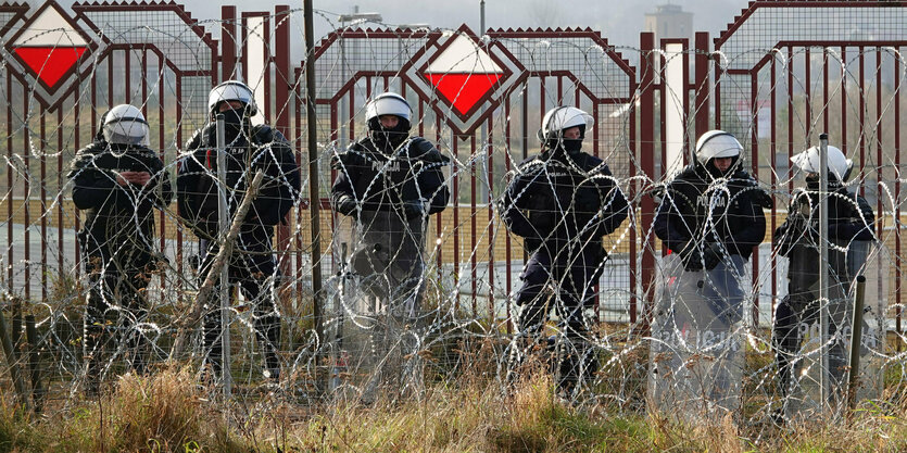 Männer in Uniform stehen hinter Stacheldraht