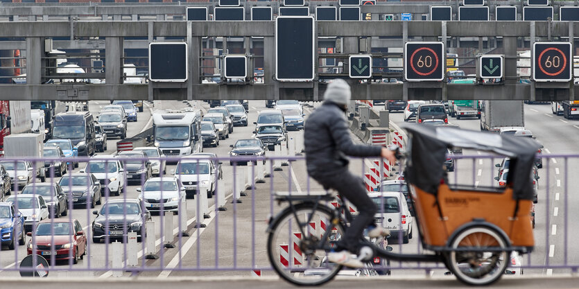 Ein Lastenrad fährt auf einer Brücke über einen Autobahnstau.