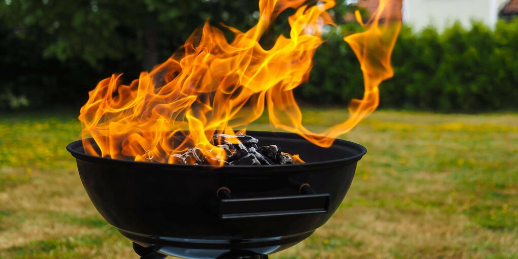 Flammen über der Holzkohle einer Grillschale im Garten