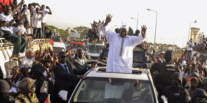 Präsident Adama Barrowbias winkt vor Menschen aus einem Autodach.