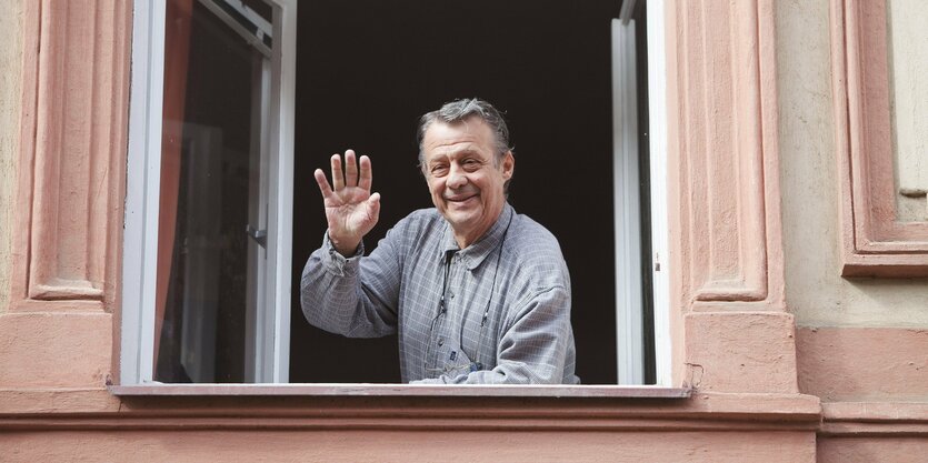 Ein Mann steht am Fenster und winkt mit der rechten Hand