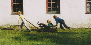 Kinder ziehen mit einem Bollerwagen um ein Haus herum