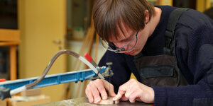 Ein Mann ein einer Werkstatt für Menschen mit Behinderung bearbeitet mit einer elektrischen Säge ein Stück Holz