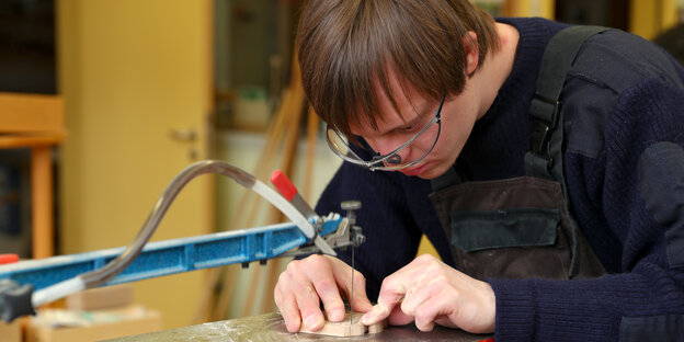 Ein Mann ein einer Werkstatt für Menschen mit Behinderung bearbeitet mit einer elektrischen Säge ein Stück Holz