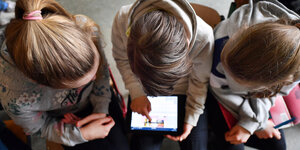 Drei Schülerinnen schauen auf ein Tablet