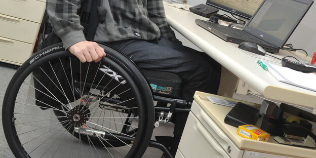 Ein Rollstuhlfahrer sitzt an seinem Bürotisch
