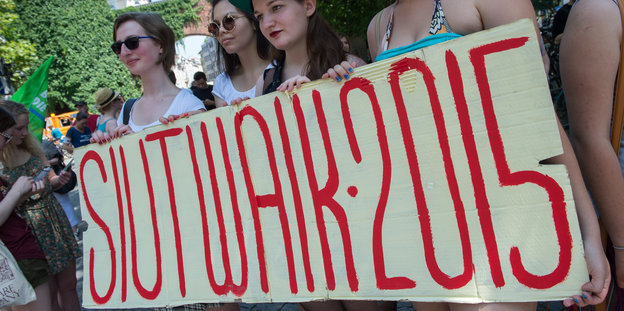 Junge Frauen halten ein Schild mit der Aufschrift "Slutwalk 2015" vor sich.