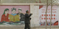 Ein chinesischer Bauer geht an einer bemalten Mauer entlang.