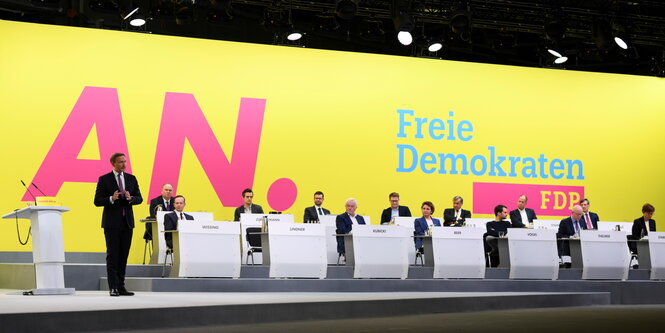 Lindner spricht, weitere Menschen sitzen auf dem Podium vor einer gelben Wand