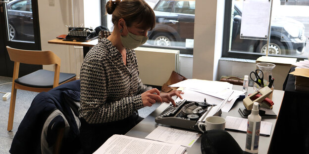eine junge Frau sitzt am Schreibtisch und tippt auf einer Schreibmaschine