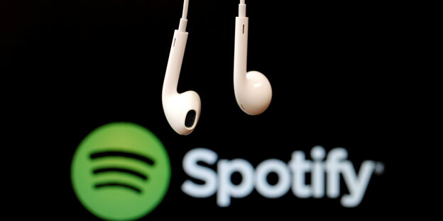 Kopfhörer hängen vor einem schwarzen Hintergrund mit dem grünen Spotify-Logo